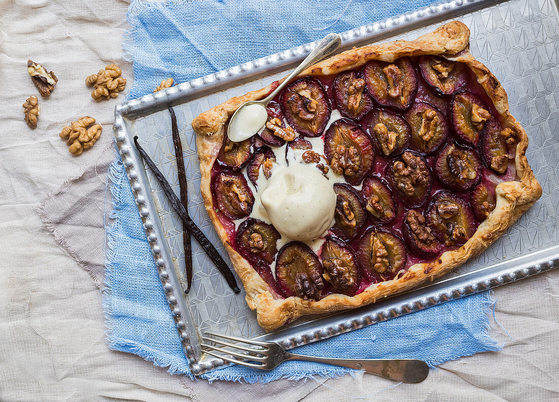 Rustic plum pie with walnuts and ice-cream on a silver tray over pieces of linen fabric