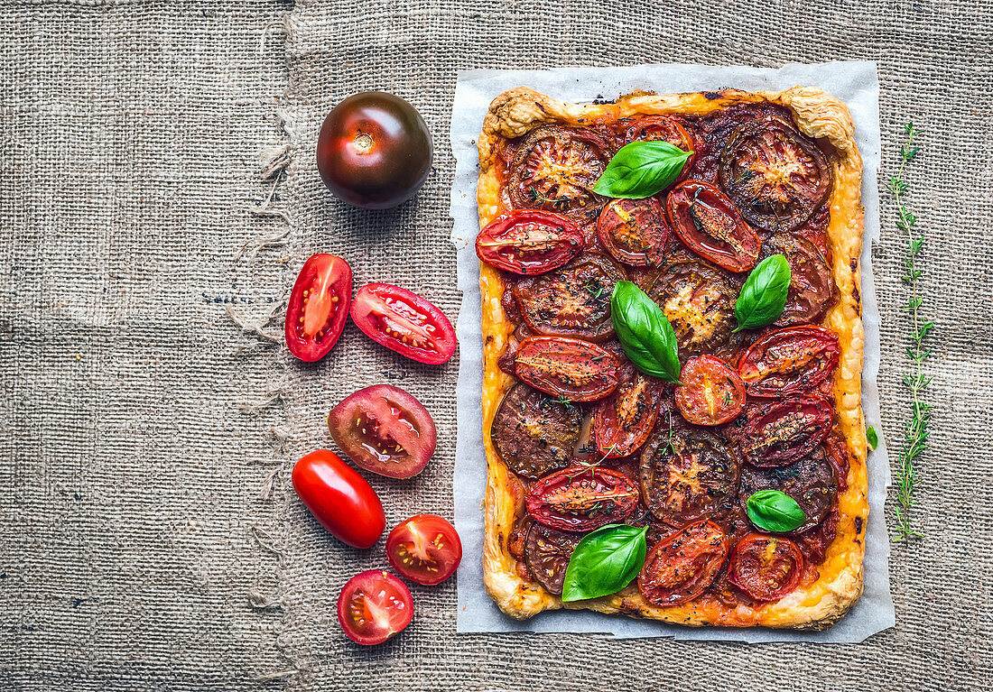 Rustic tomato autumn pie with fresh basil, thyme and tomatoes on a silver tray over a sackcloth background