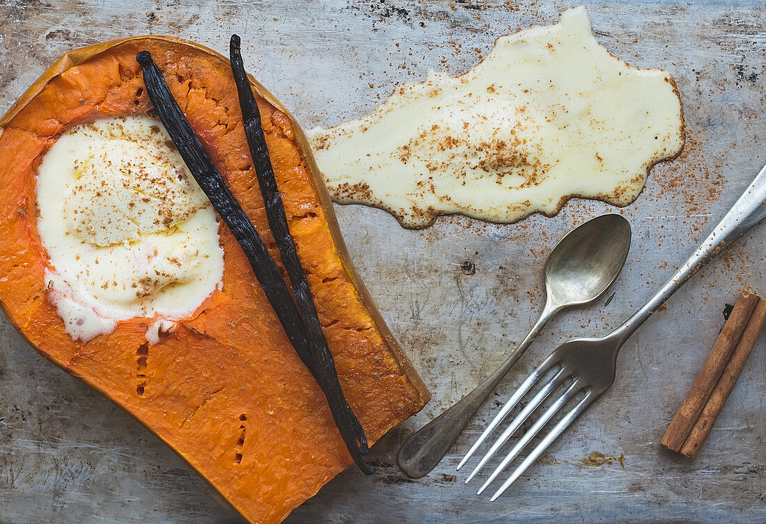 Backed pumpkin half with a scoop of vanilla ice-cream, vanilla sticks, cinnamon, a fork and a tea-spoon