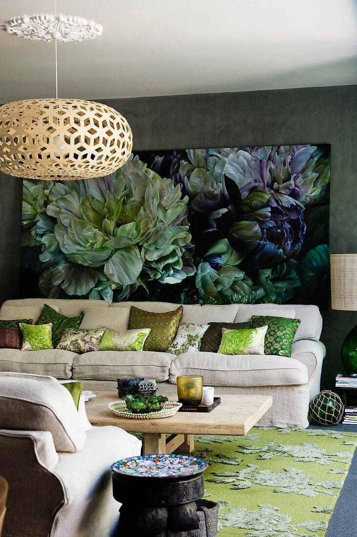 Wooden table and pale sofa set with scatter cushions in front of large painting in living room