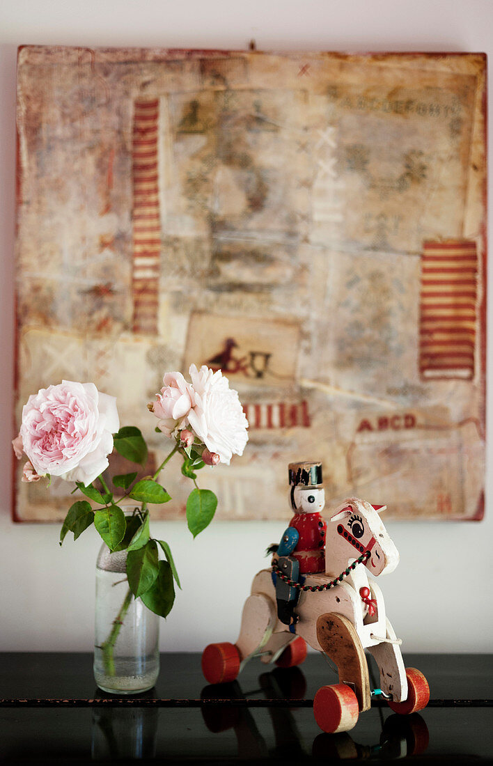 Vintage knight-and-horse toy and pink roses in front of collage