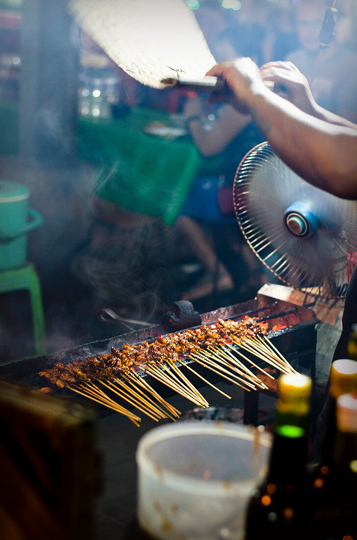 Satay sticks on the grill being fanned at a market in Bali