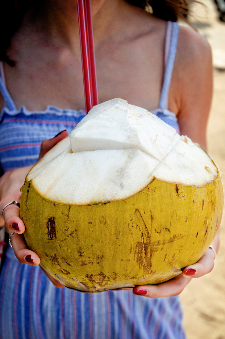 Frau hält frische Kokosnuss mit Strohhalmen