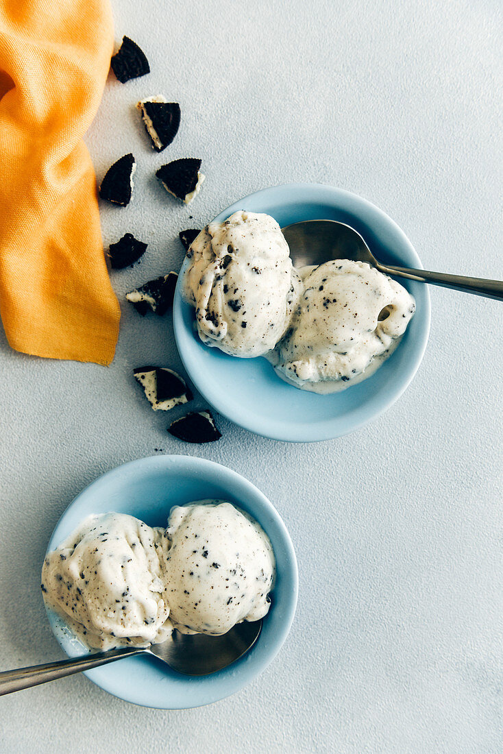 Chocolate cookie ice cream in two blue bowls with a spoon on the side