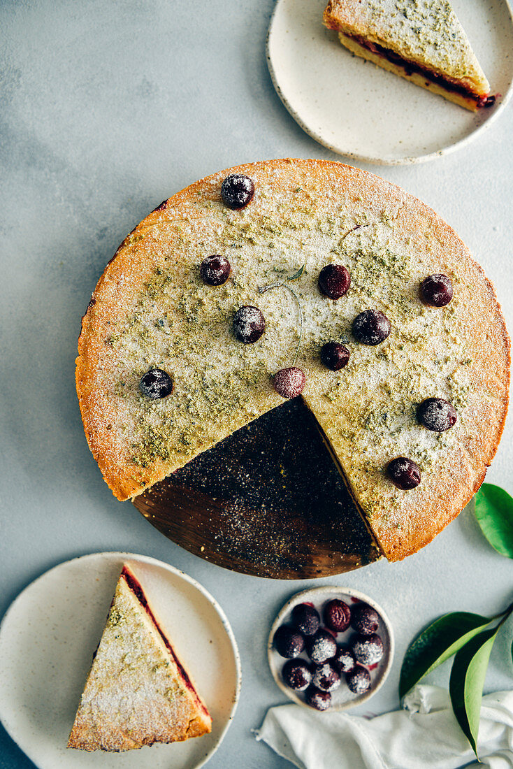 A cherry pie topped with a single cherry, pistachio and powdered sugar sliced