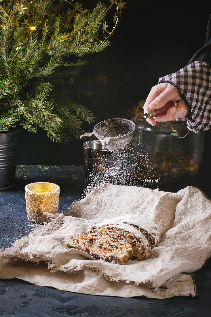 Stollen on linen napkin with sprinkling sugar powder by vintage sieve in child hand