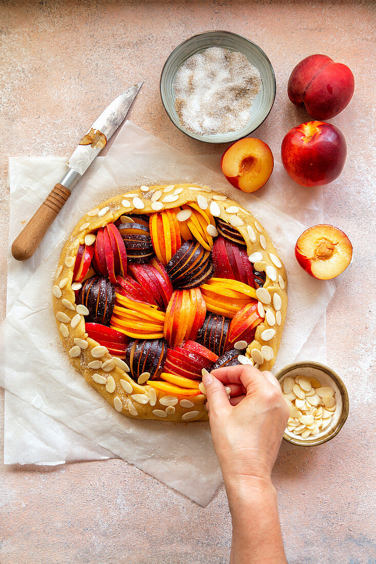 Preparing a stone fruit galette.Hand sprinkles almond flakes over the crust