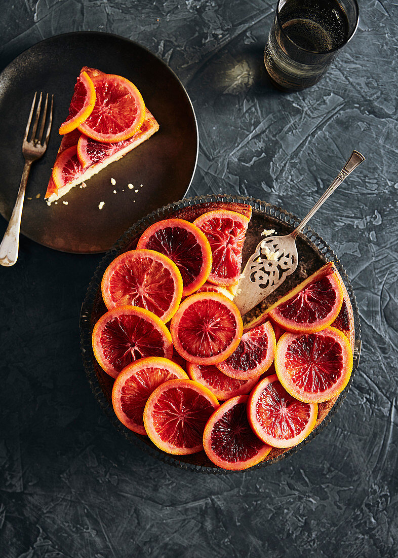 Moody blood orange cake with slices of poached blood oranges on top in a sugar syrup