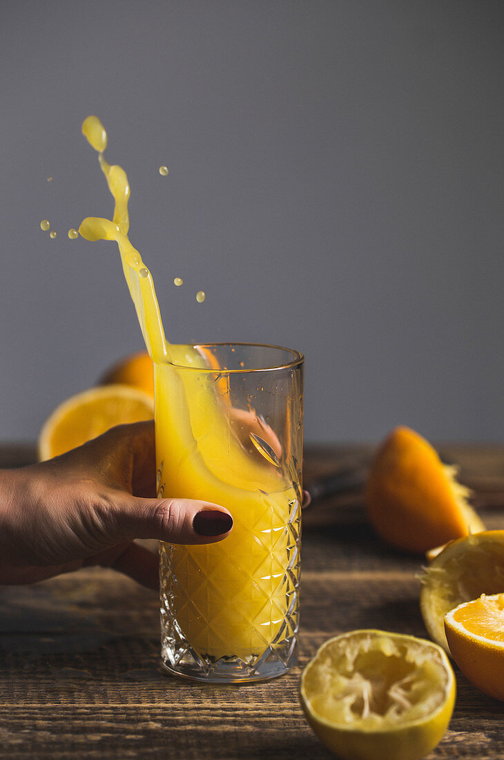 A woman holding a splashing glass of freshly pressed orange juice