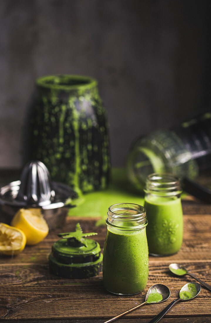Freshly mixed green smoothies in screw-top jars with a blender in a background