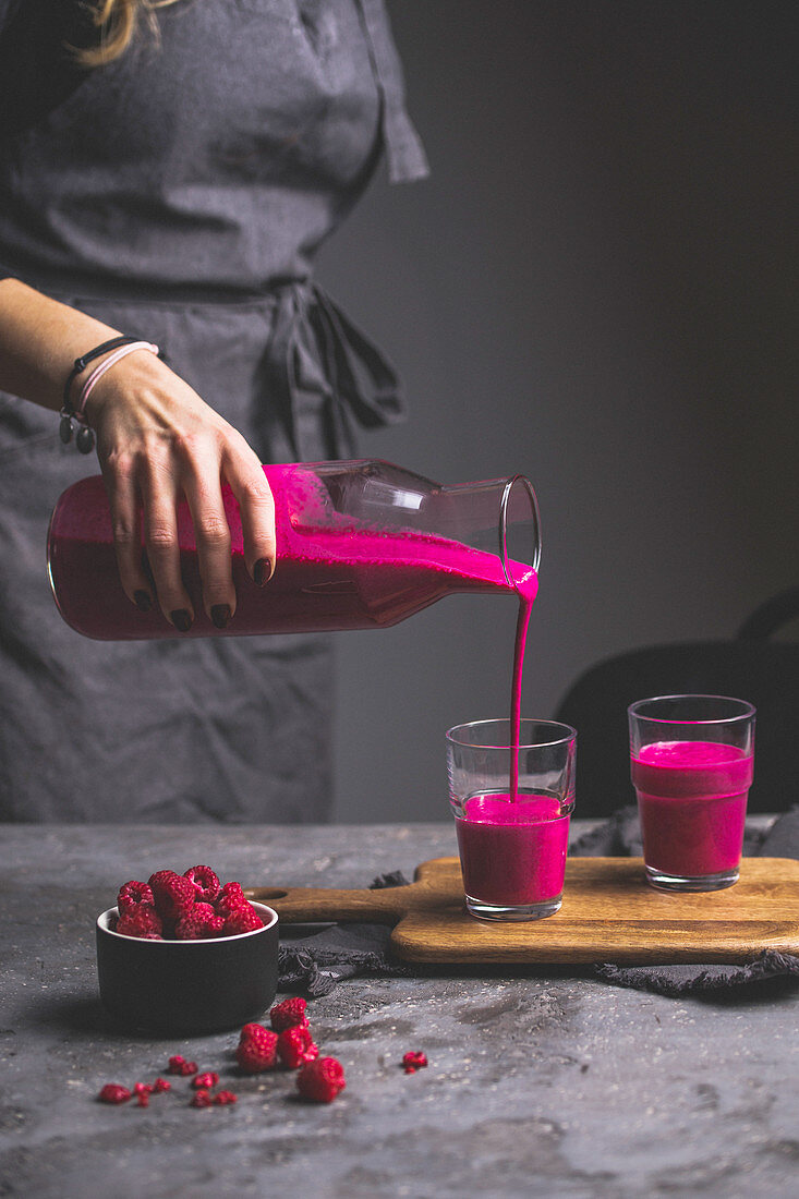 A woman pouring a pink smoothie from a carafe into glasses