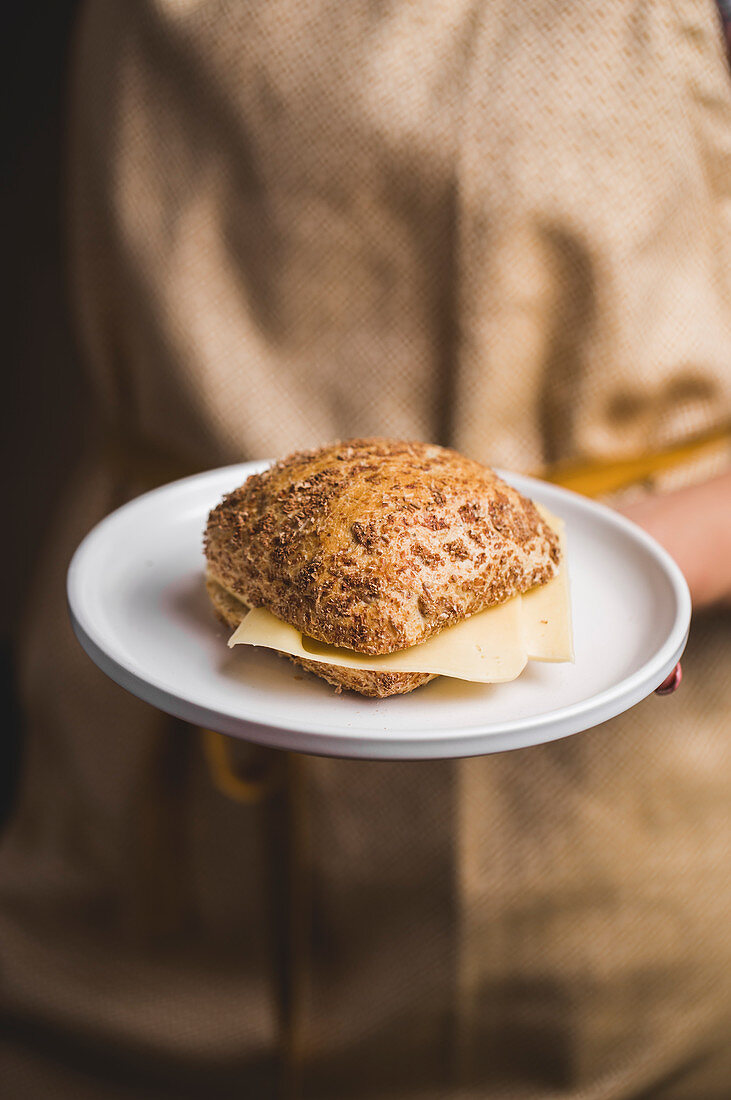 A person holding a cheese roll on a plate