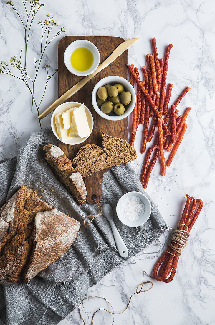 Brot serviert mit Butter, Oliven, Olivenöl, Salz und Minisalamis (Aufsicht)