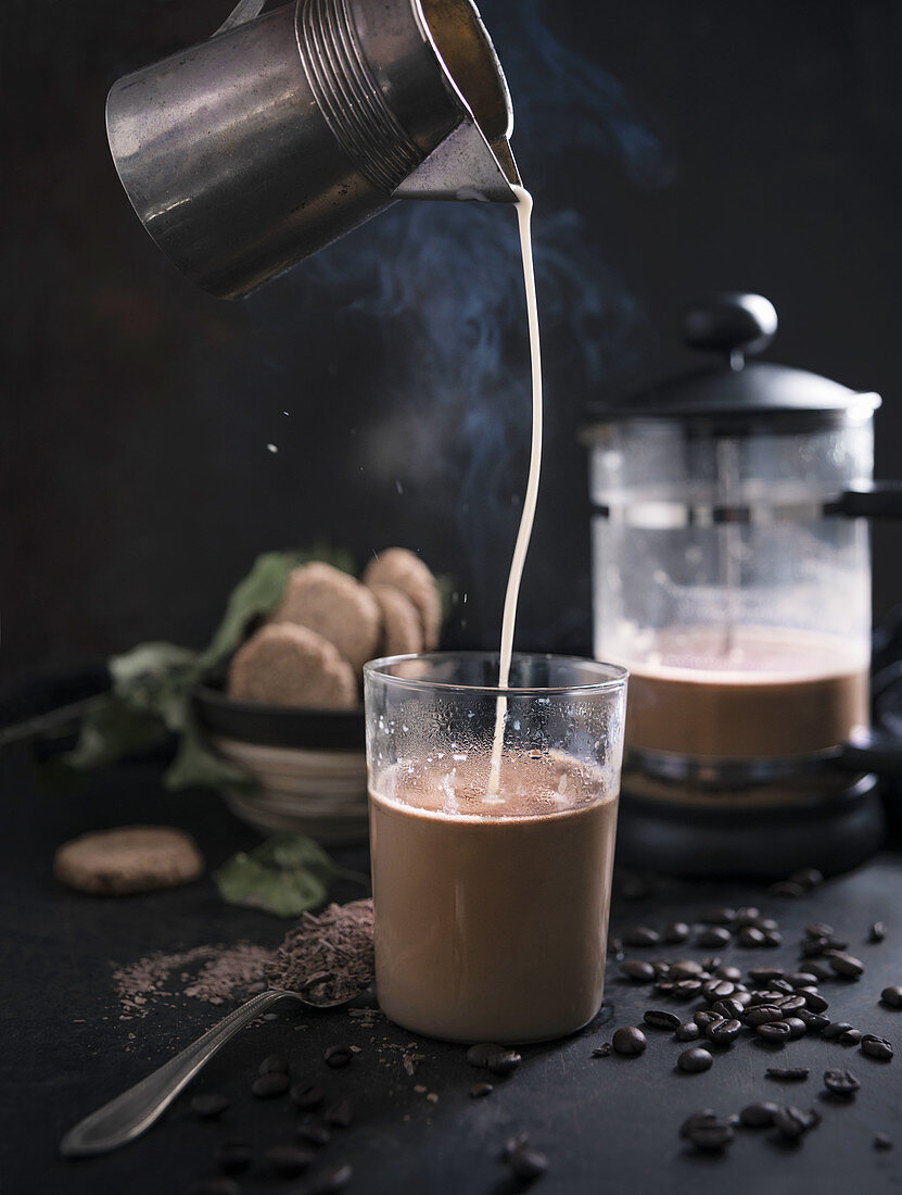 Oat milk being poured into a hot drink made of cocoa and chocolate