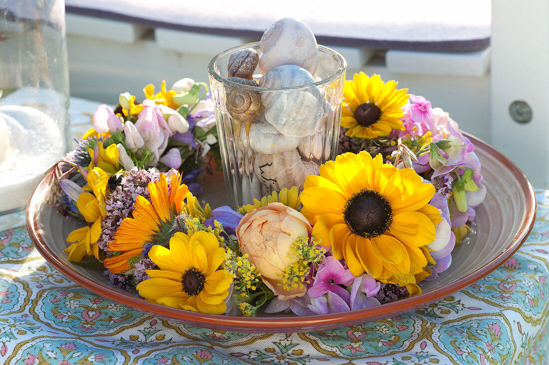 Glass with snail shell in a wreath of flowers