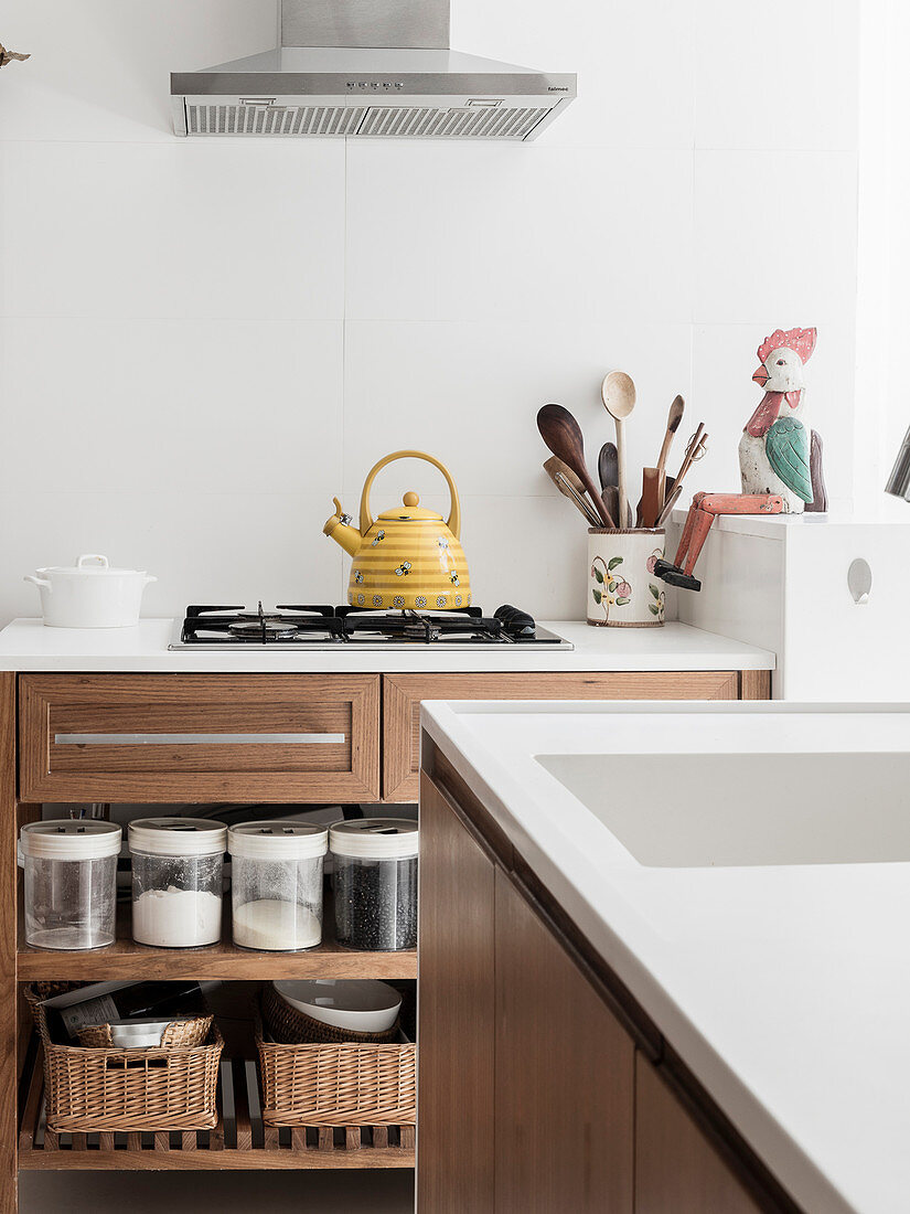 Storage jars on base-unit shelves and kettle on gas hob seen across island counter