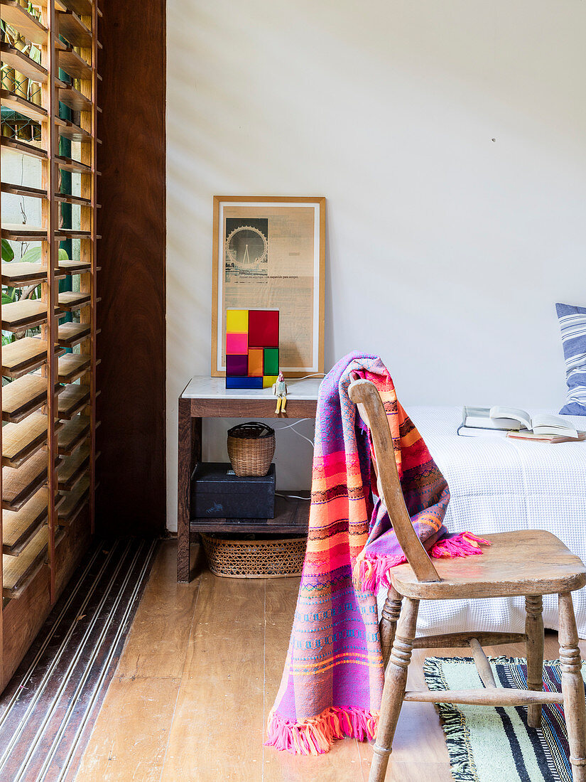 Colourful blanket on rustic wooden chair next to window with louvre blinds