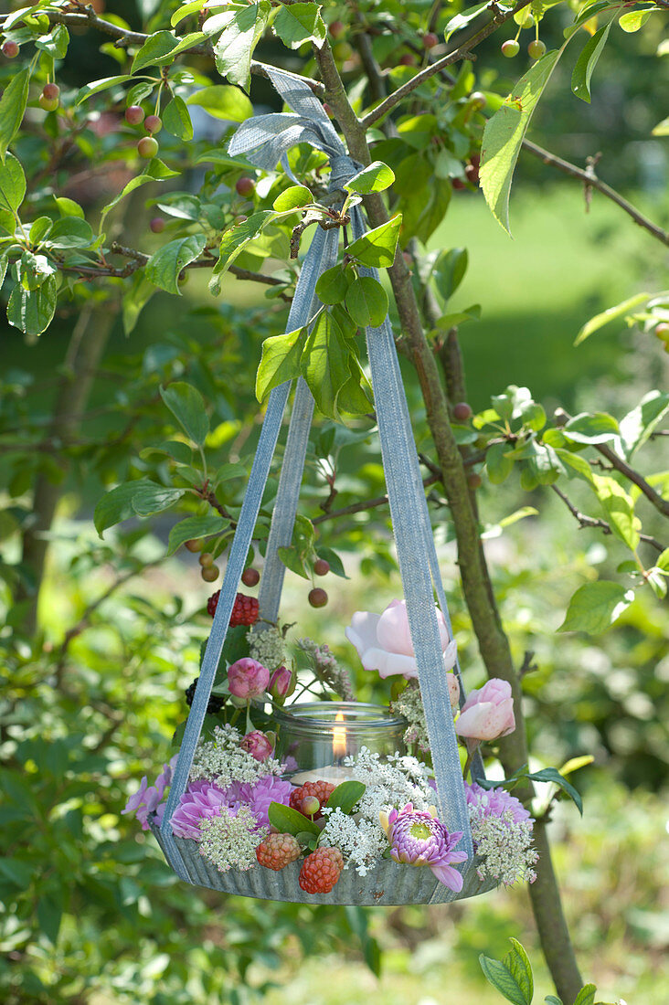 Flower wreath with wind light in a baking pan hung from a decorative apple tree