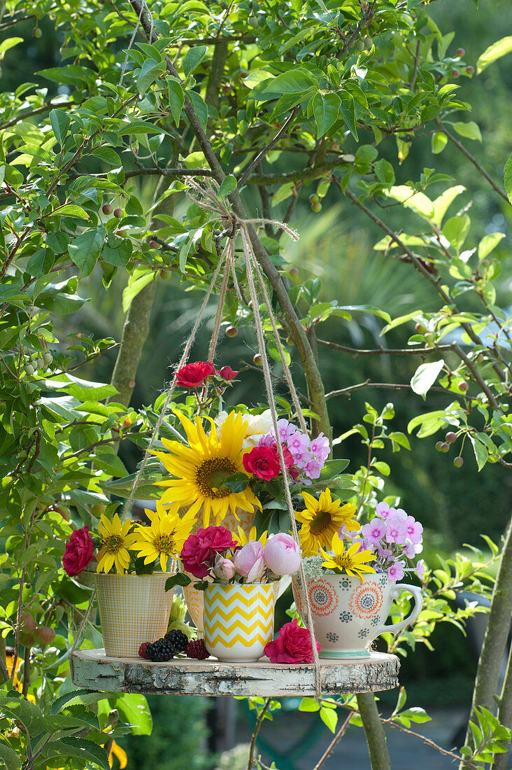 Small bouquets of sunflowers, roses and phlox in cups on a wooden disc