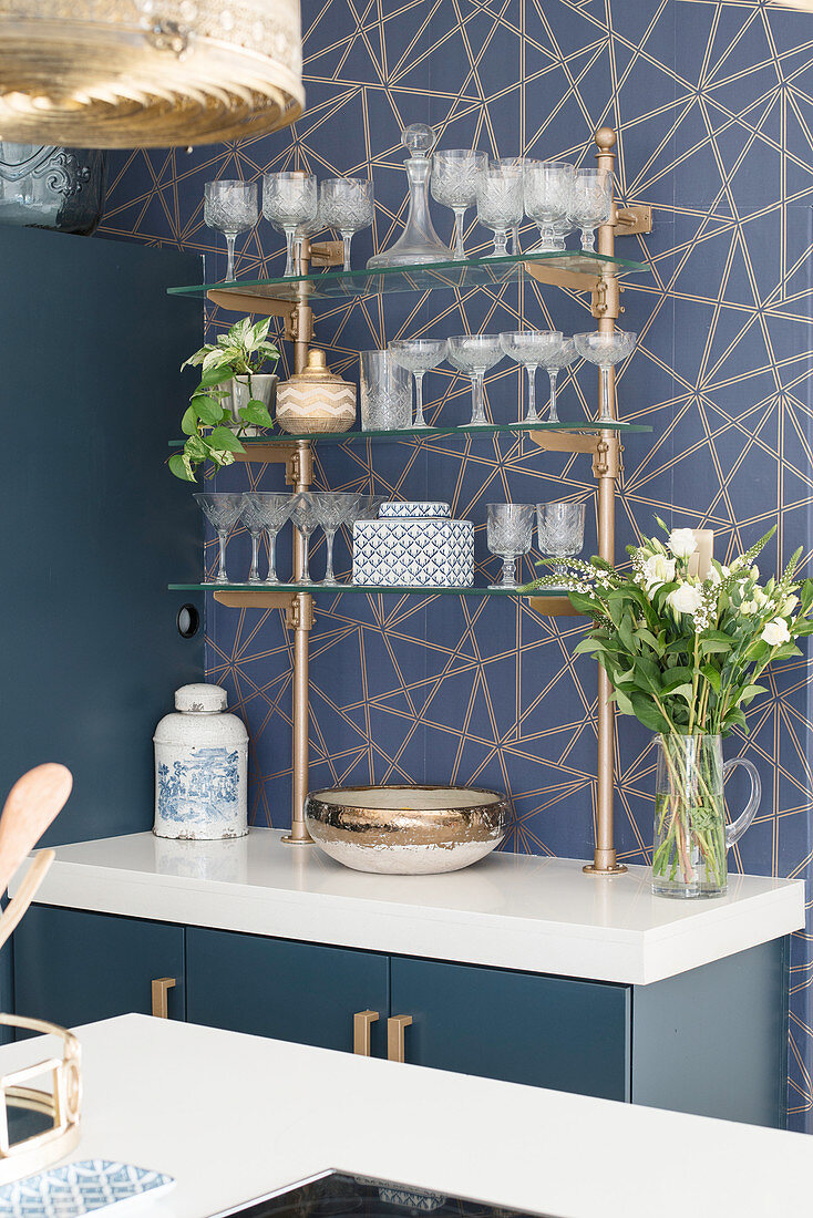 Vintage-style glasses on bar shelves against blue-and-gold patterned wall