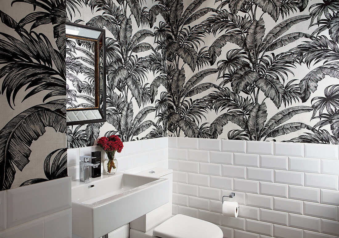 Leaf-patterned wallpaper and white wall tiles in guest toilet