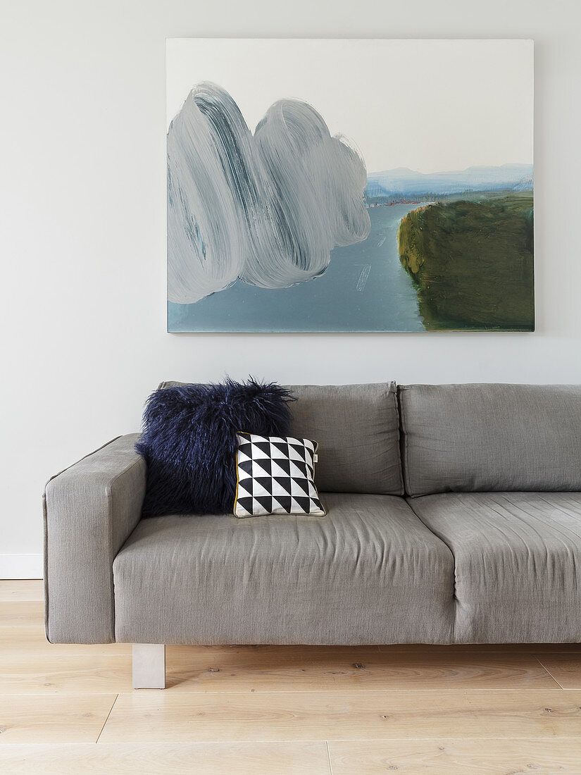 Scatter cushions on grey sofa below picture in living room