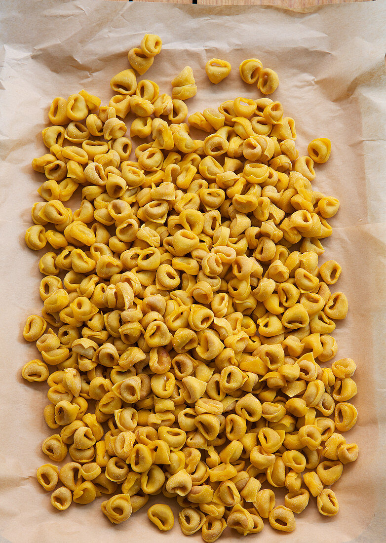 Viele ungekochte Tortellini auf Papier (Aufsicht)