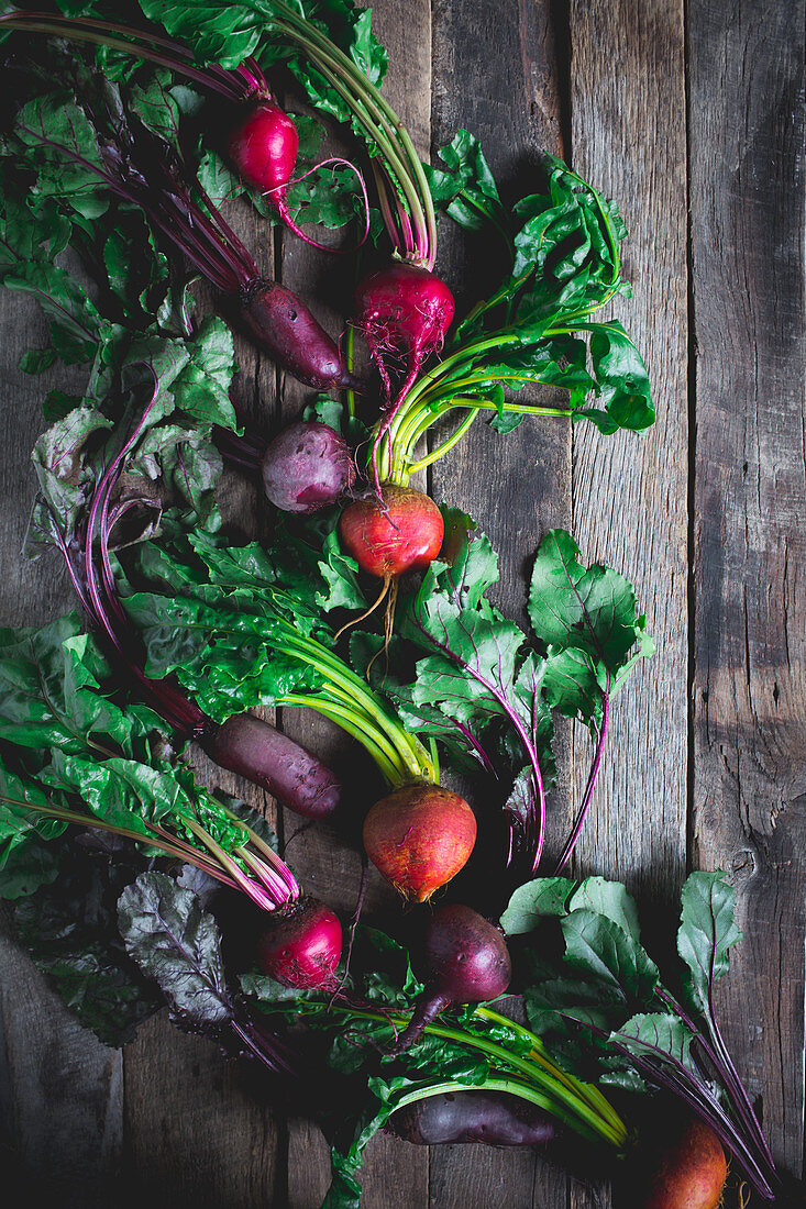 Golden, red, and purple beets on a rustic wood shooting surface with greens attached