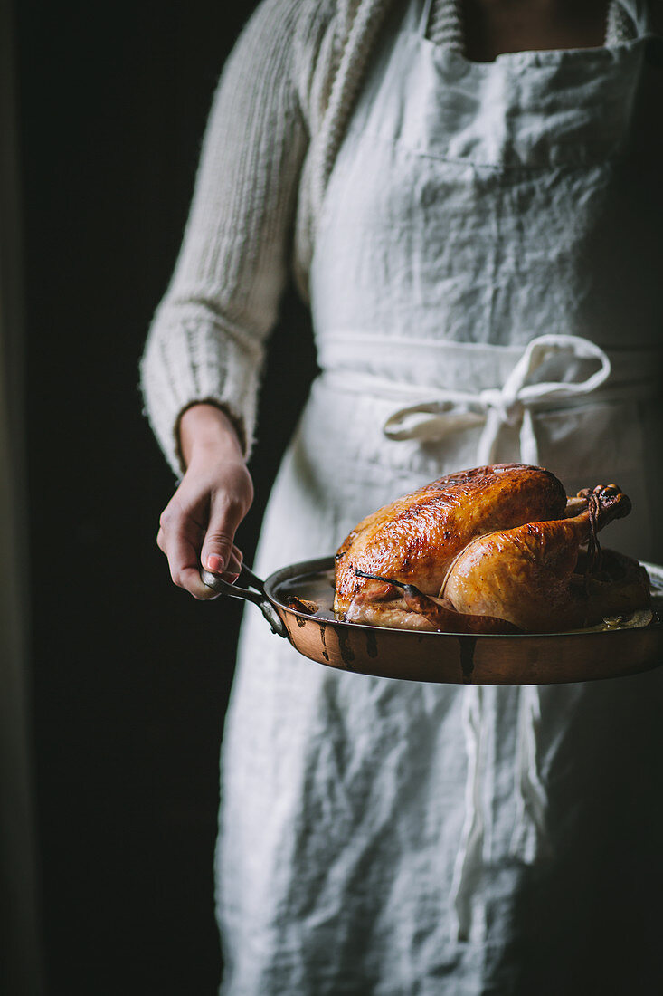 A golden roast chicken with an apple and pear glaze in a copper roasting pan on a rustic wood tabletop