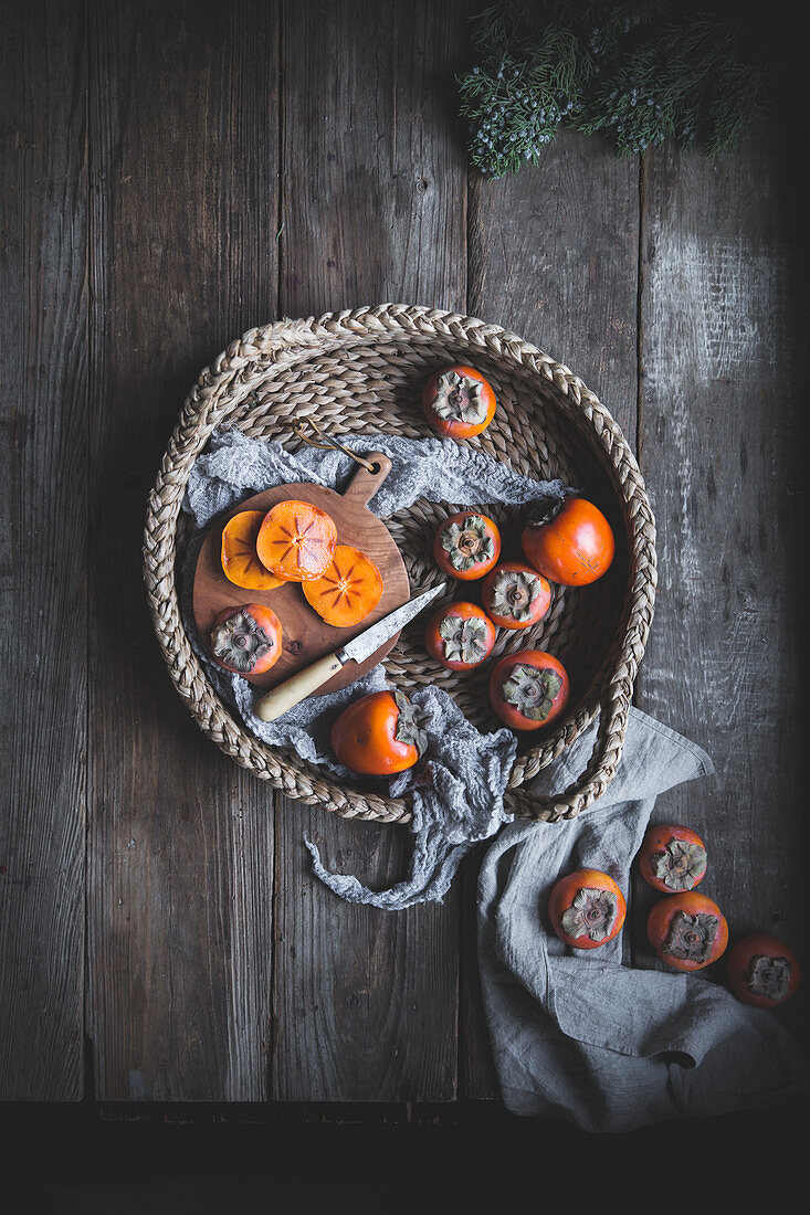 Persimmons on a rustic wood table top in a woven wicker basket