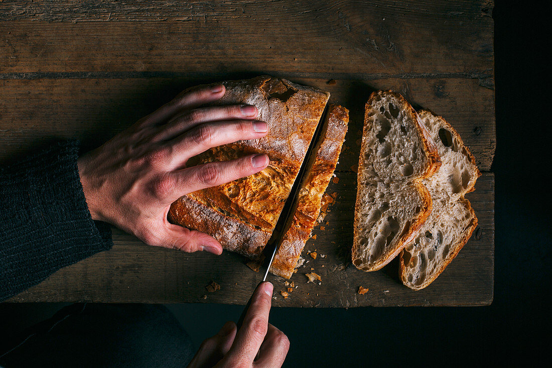 Hände schneiden Brot auf Holztisch