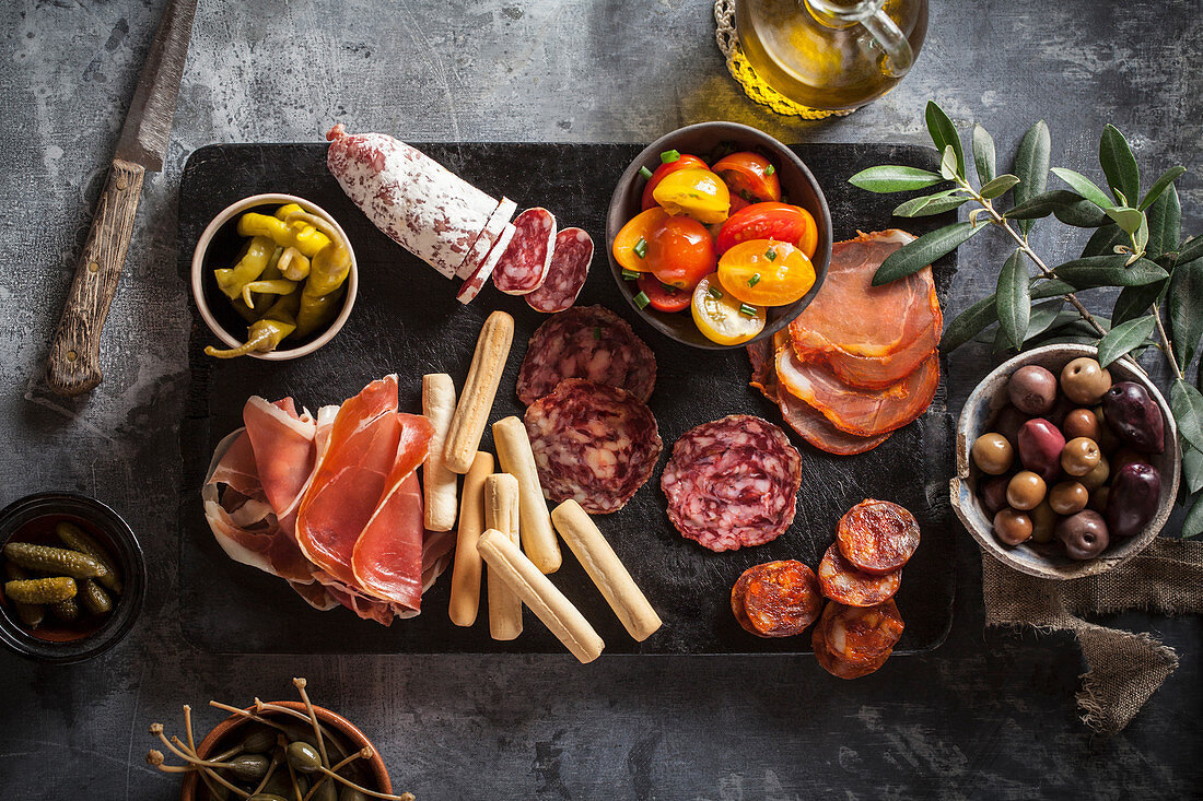 An appetizer platter with ham, salami, tomatoes, olives and hot peppers