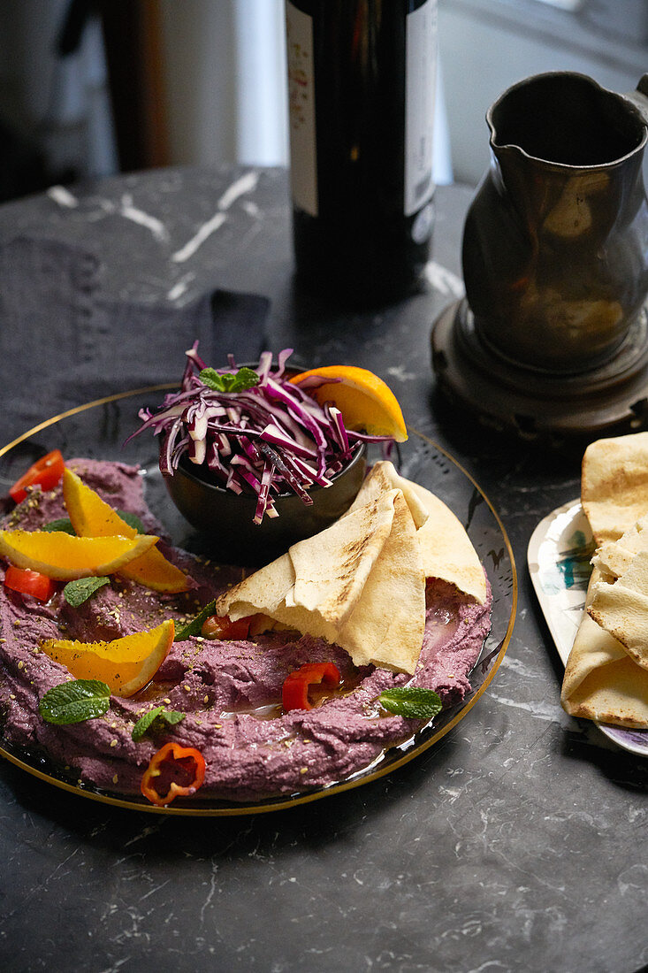 A purple dip with flatbread, oranges and vegetables
