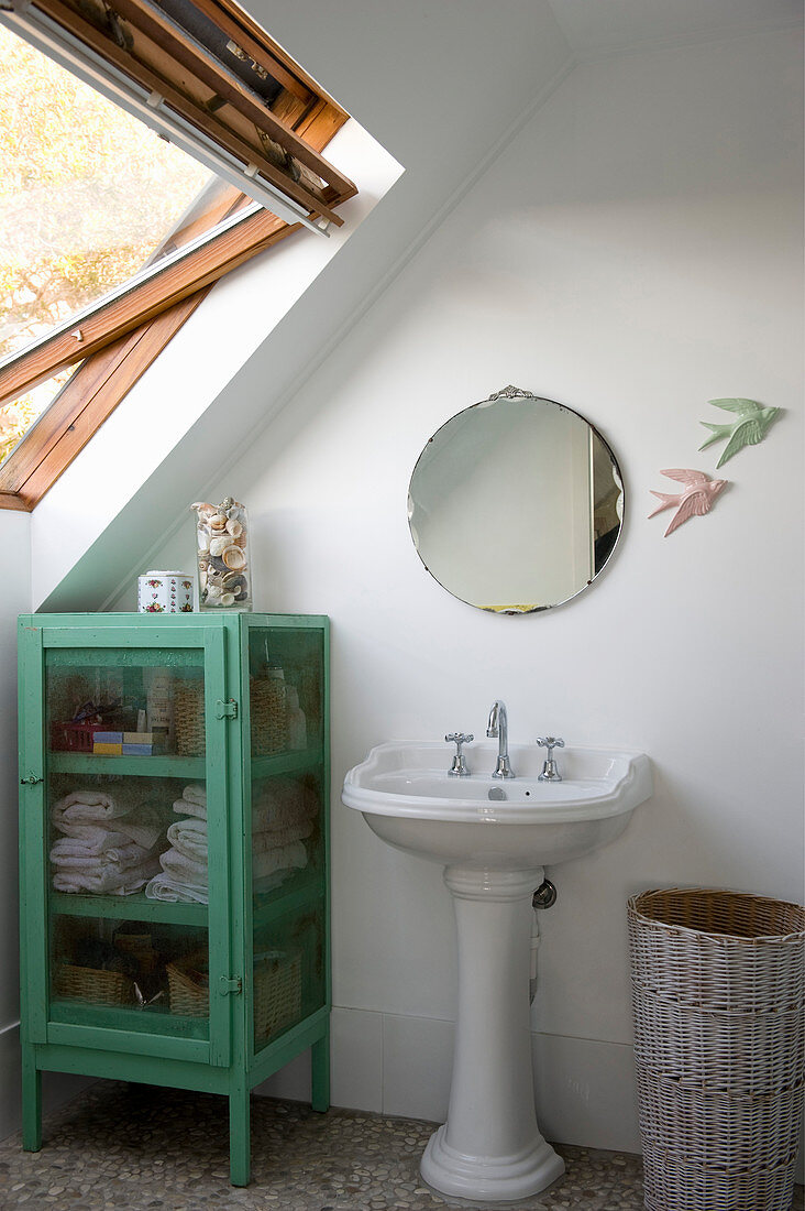 Vintage-style pedestal sink and green glass-fronted cabinet under sloping ceiling