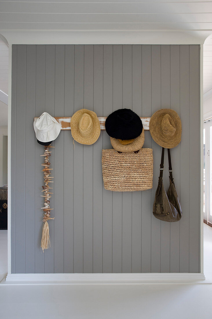 Summer hats and bags on coat rack on grey board wall