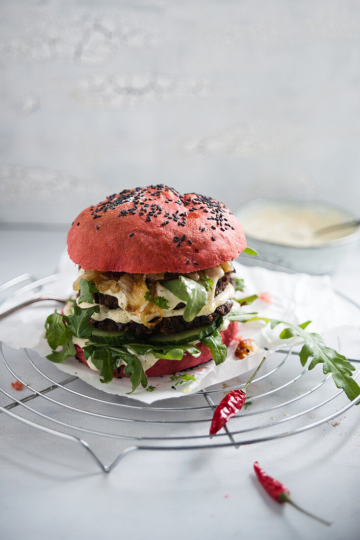 A burger with a beetroot bun, a black-bean patty, rocket, cucumber and remoulade