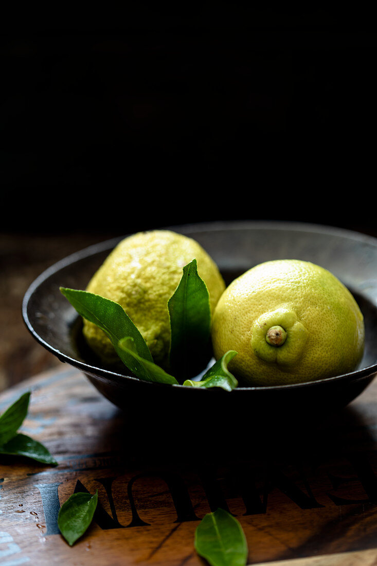 Two lemons with leaves in a bowl