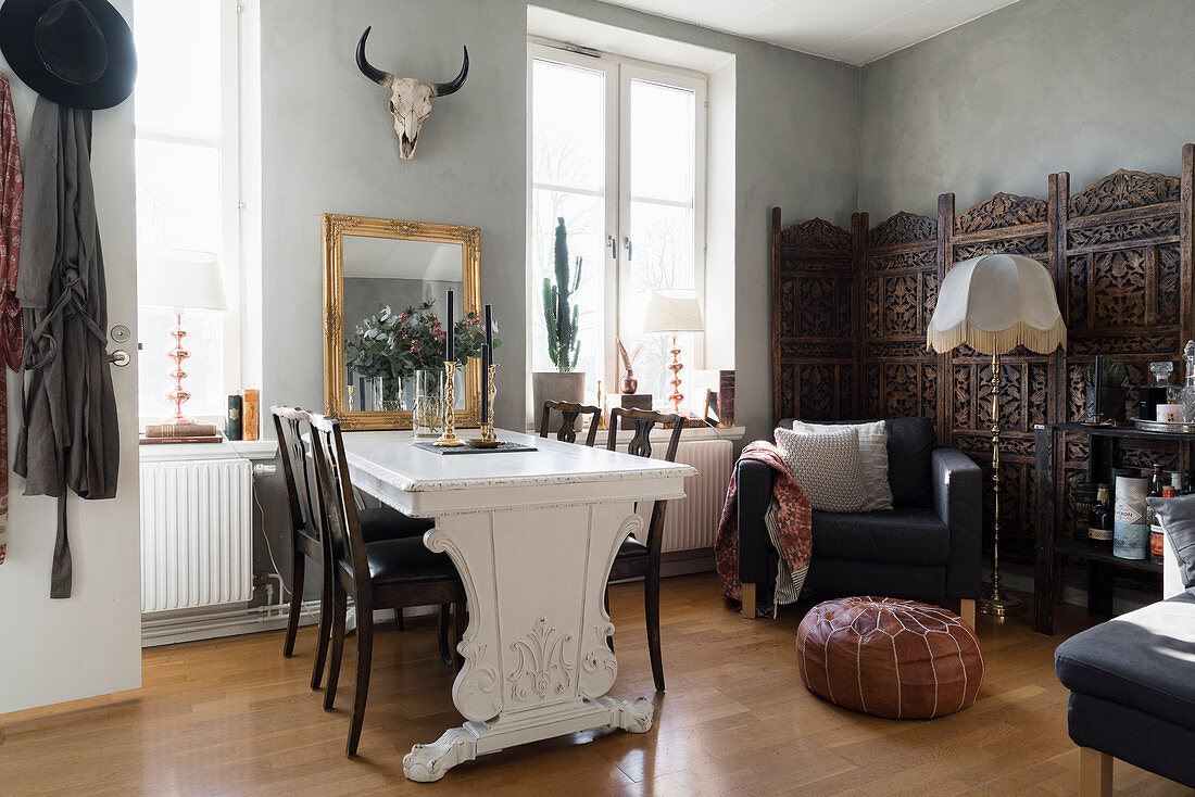 Dining table and chairs, armchair and screen in open-plan interior with pale grey walls