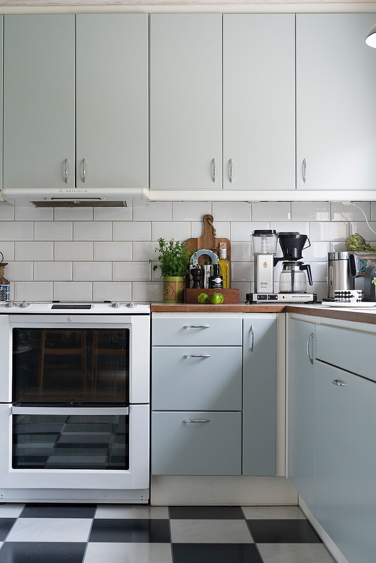 Helle Einbauküche mit weißen Wandfliesen und schwarz-weiß kariertem Linoleumboden