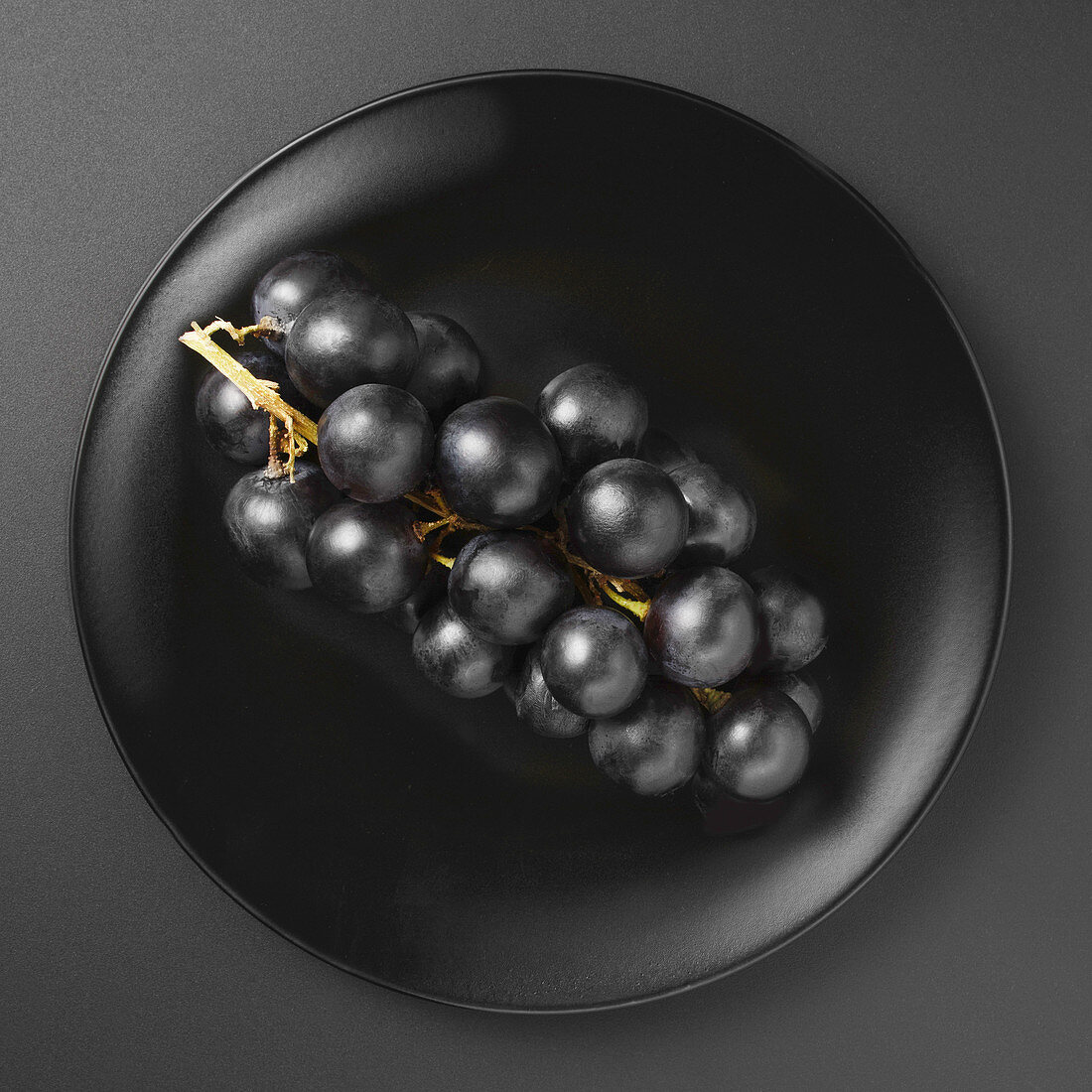 A bunch of black grapes on a black matte plate on a black background
