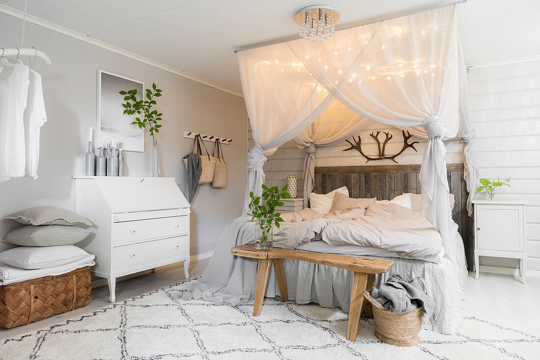 Double bed below canopy with lights, wooden bench and bureau in pale bedroom