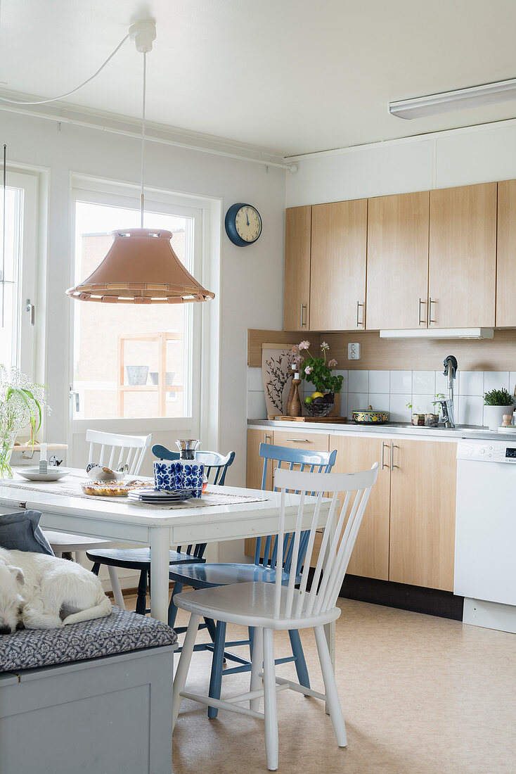 Dining table with chairs and bench in kitchen-dining room with pale cupboards