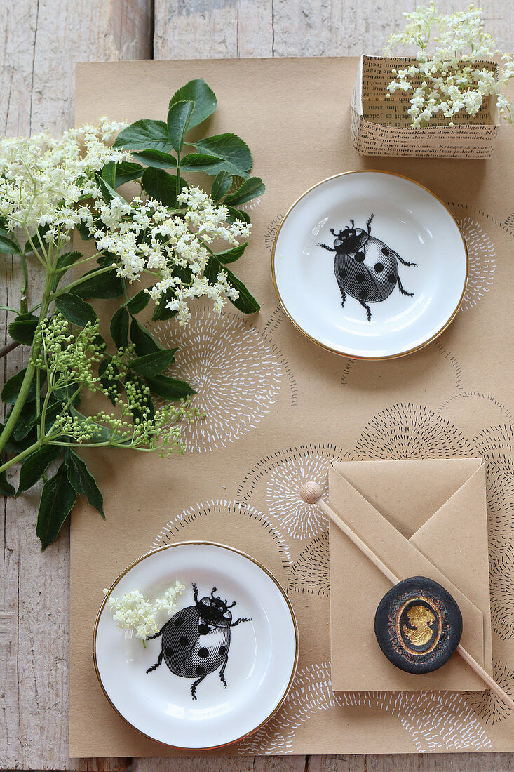 Still-life arrangement with elderflowers, plates with ladybird motifs and paper crafts