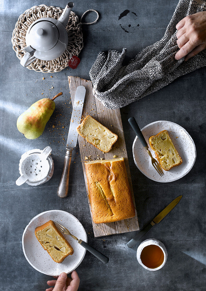 Kastenkuchen mit Birnen, angeschnitten auf Holzbrett und auf Tellern