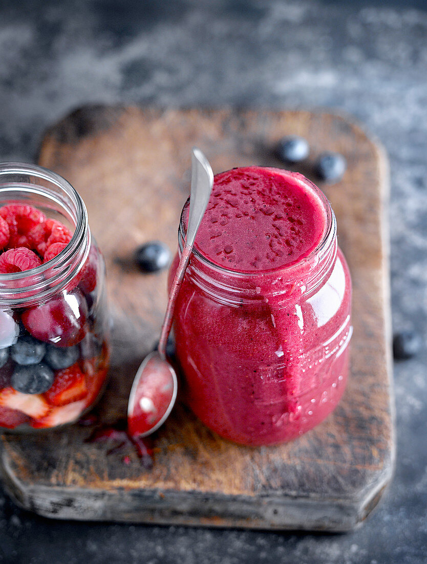 Close-up of glass jar filled up to maximum with red fruit smoothie and served with spoon on wooden board