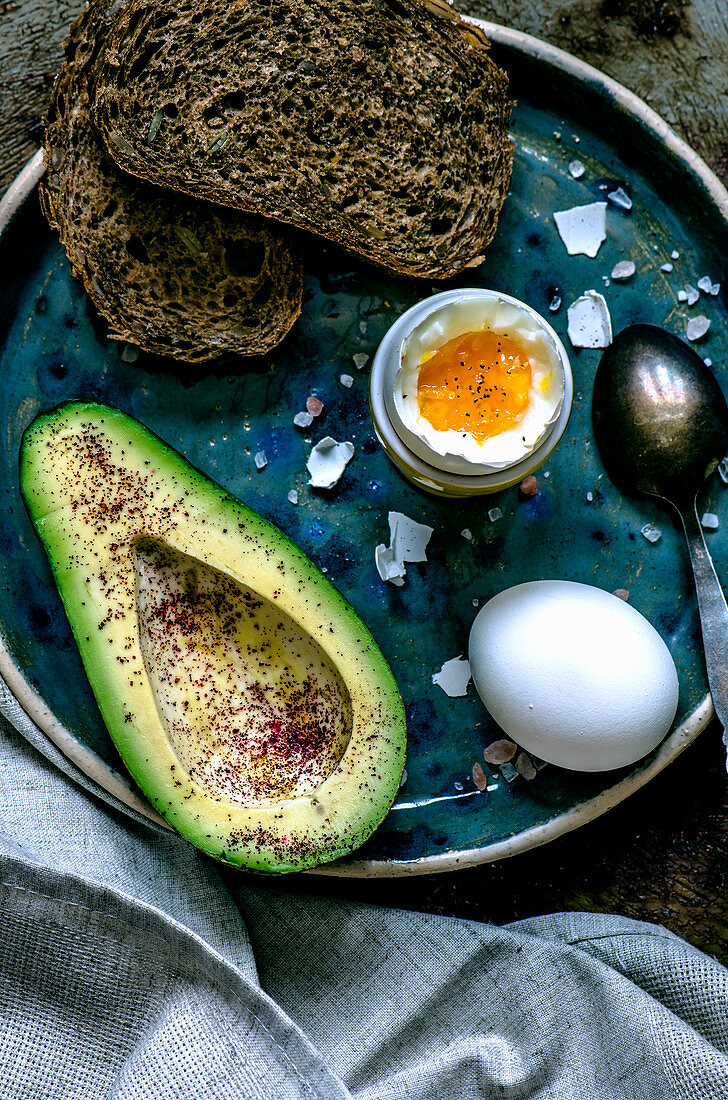 Grain bread, avacado, soft-boiled egg and Himalayan salt on a blue plate with linen napkin