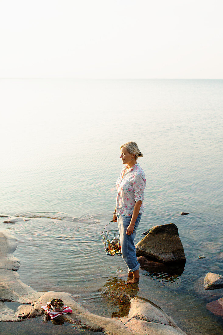 A picnic by a lake with a woman holding wine in a wire basket