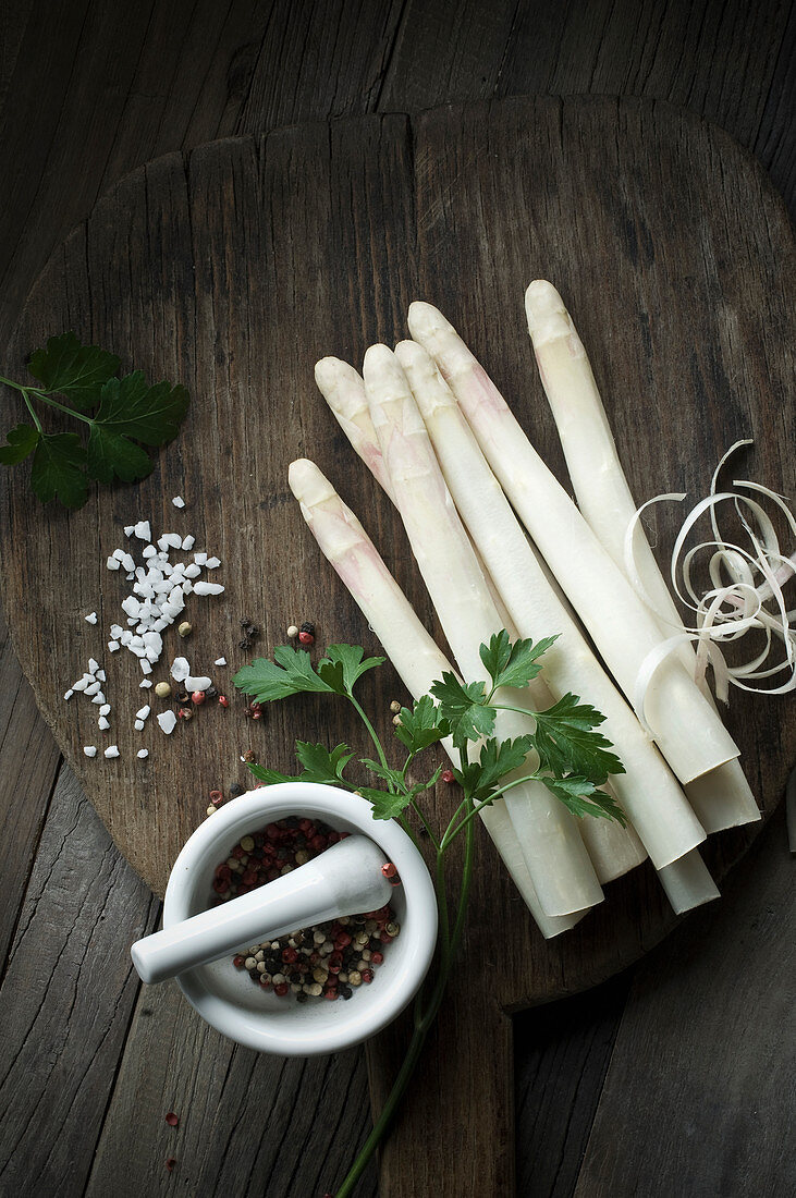 White asparagus, salt, pepper, parsley and a mortar on a wooden board