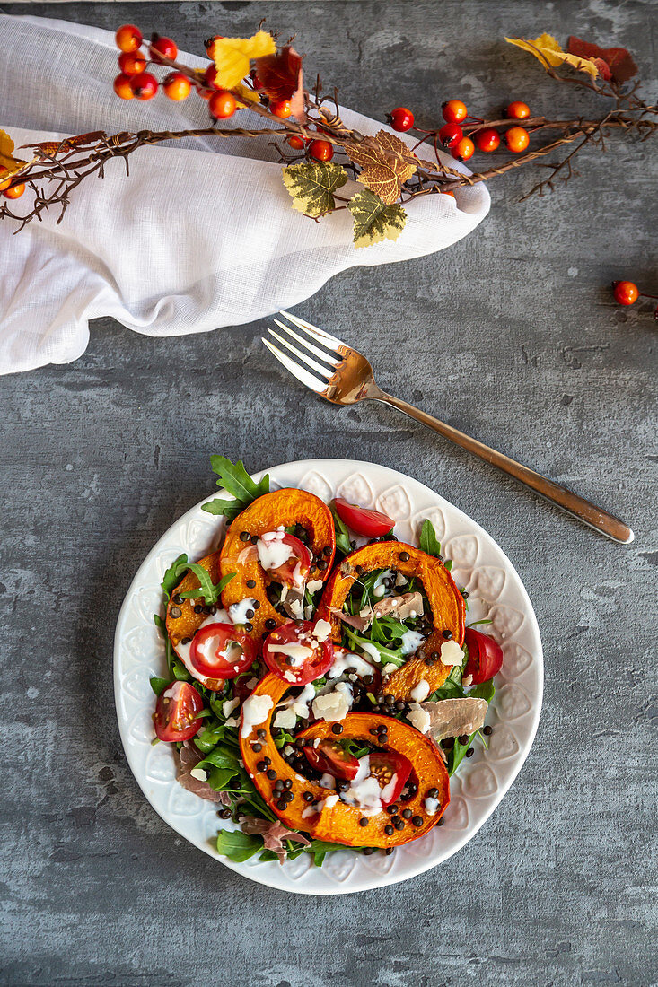 Herbstlicher Salat mit Rucola, Kürbis, Beluga-Linsen, Tomaten, Parmaschinken, Parmesan und Joghurtdressing