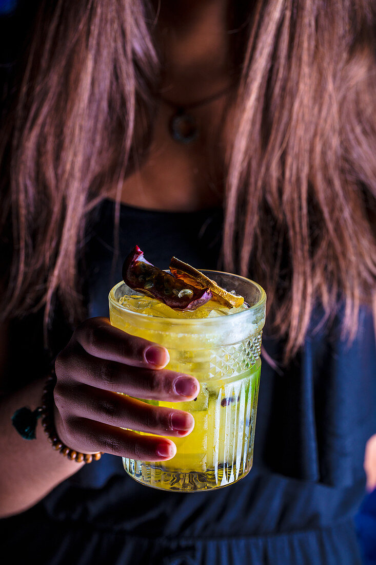 Frauenhand hält ein Glas Cocktail mit Maracuja